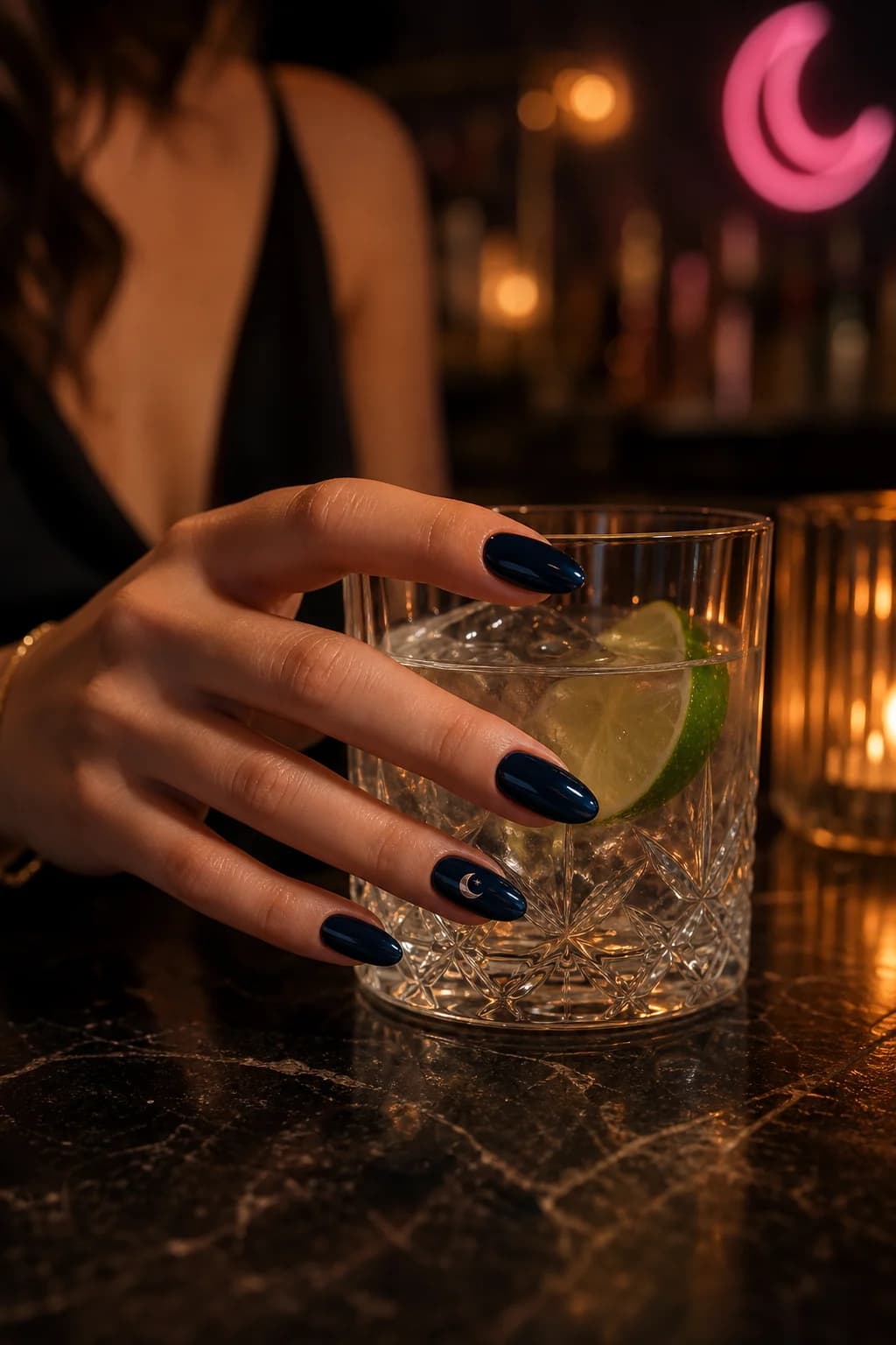 Navy almond nails holding a glass at a dark bar; one nail wears the Vesper crescent sticker
